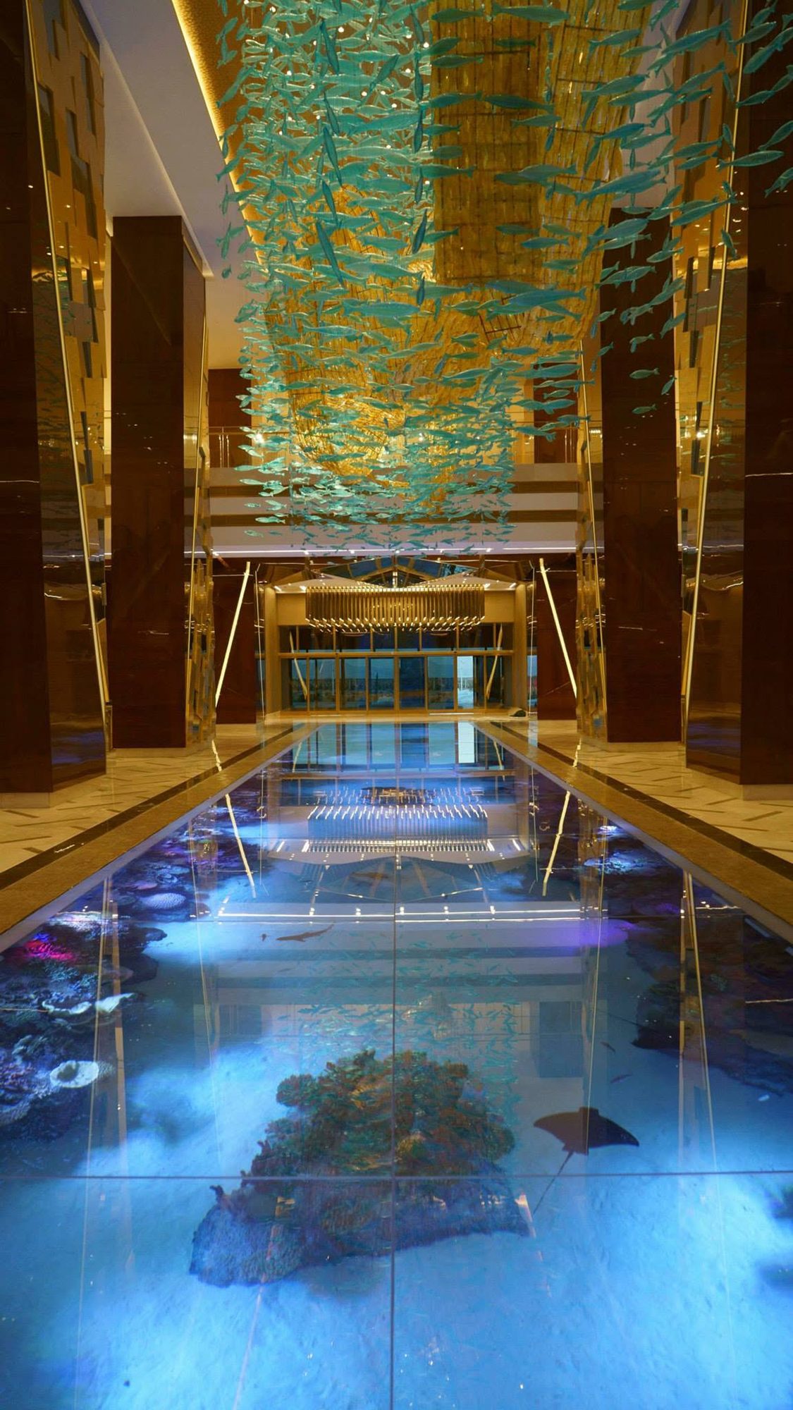 Wide view of the Avaza Congress Center ground aquarium with golden mirrored columns and a blue-lit reef floor, Turkmenistan