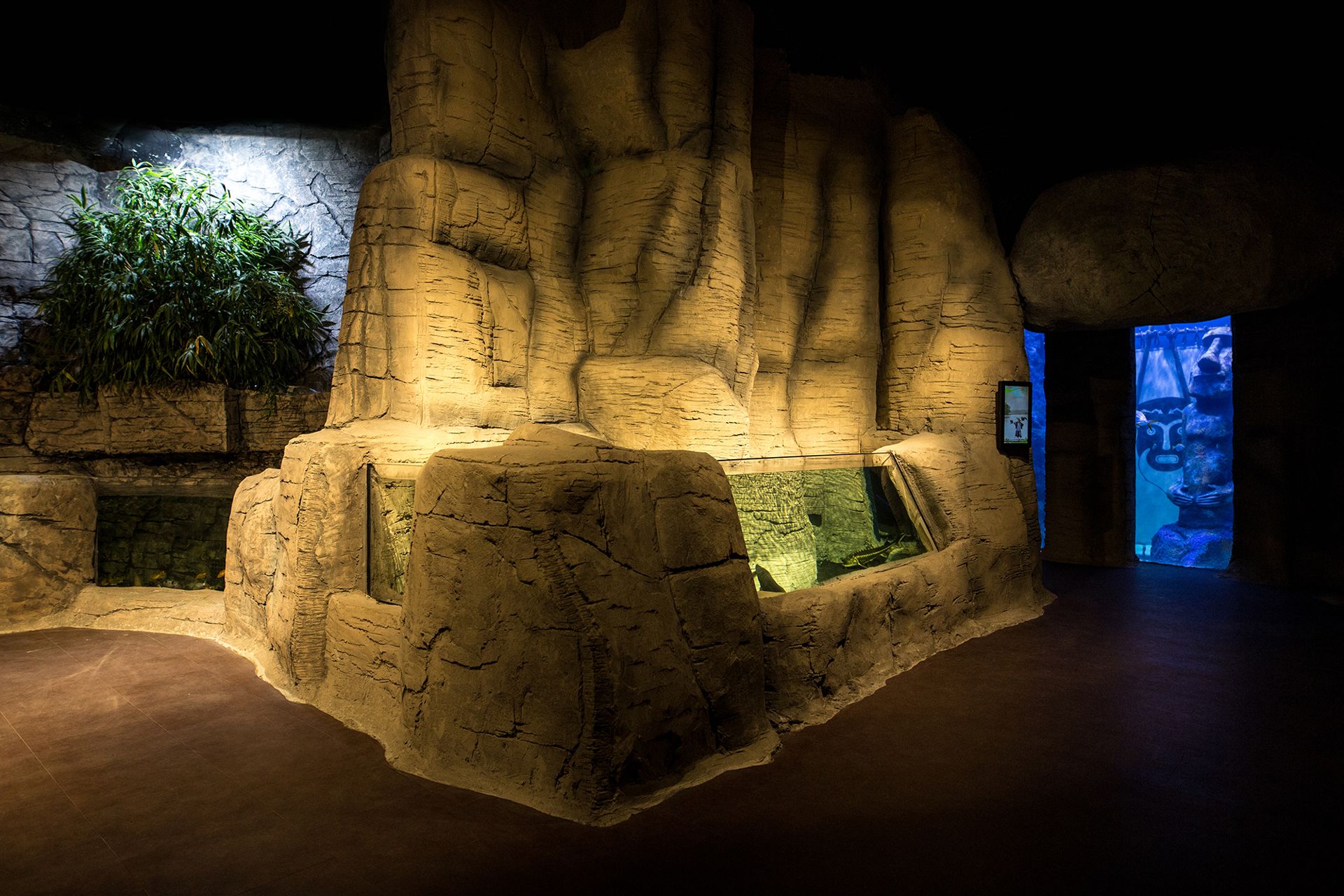 Warm-lit rocky cave exhibit with bamboo and a moai-statue doorway at İzmir Funtastic Aquarium