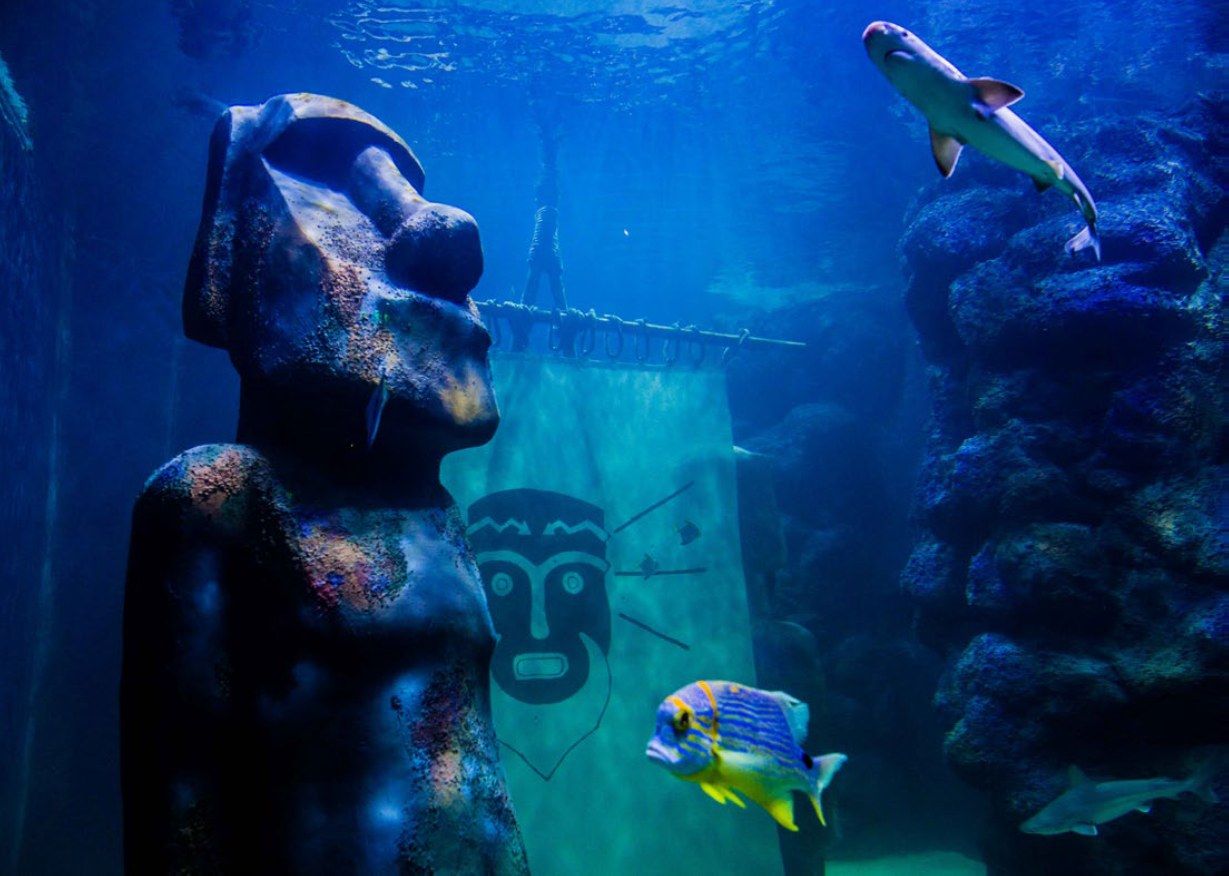 Underwater moai statue with a tribal banner and a shark at İzmir Funtastic Aquarium, Türkiye